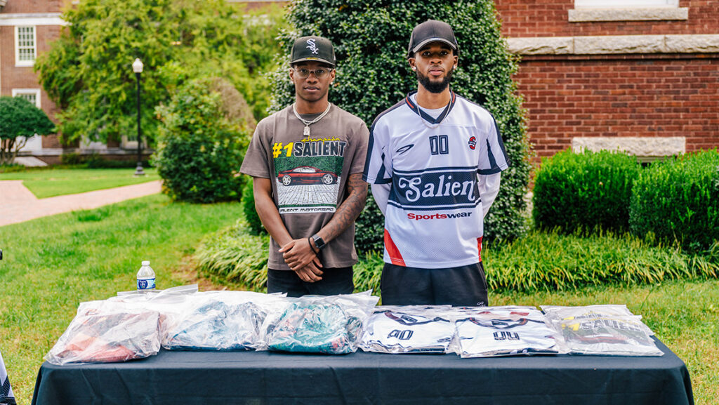 Two UNCG students stand in front of the jerseys they are selling outside.