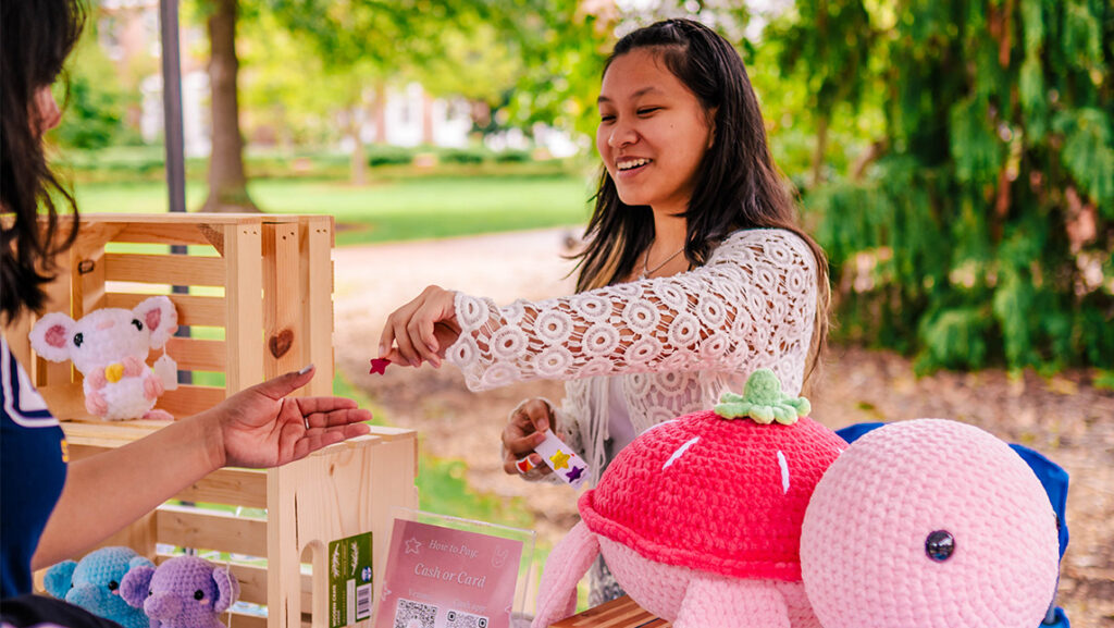 A UNCG student entrepreneur gives a customer a piece of jewelry.